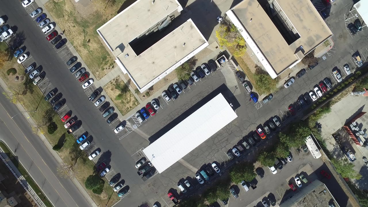 Top-down aerial frame over Hidden Lake, Colorado showing rows of parked cars beside flat-roof buildings, a street edge, dry grass, trees, and no visible people.
