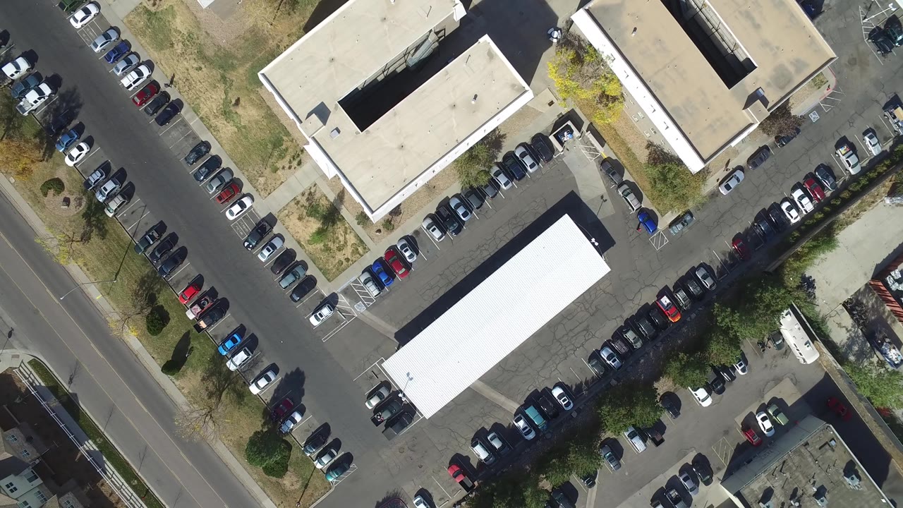 Top-down view of a street, parking areas, rooftops, and scattered trees.