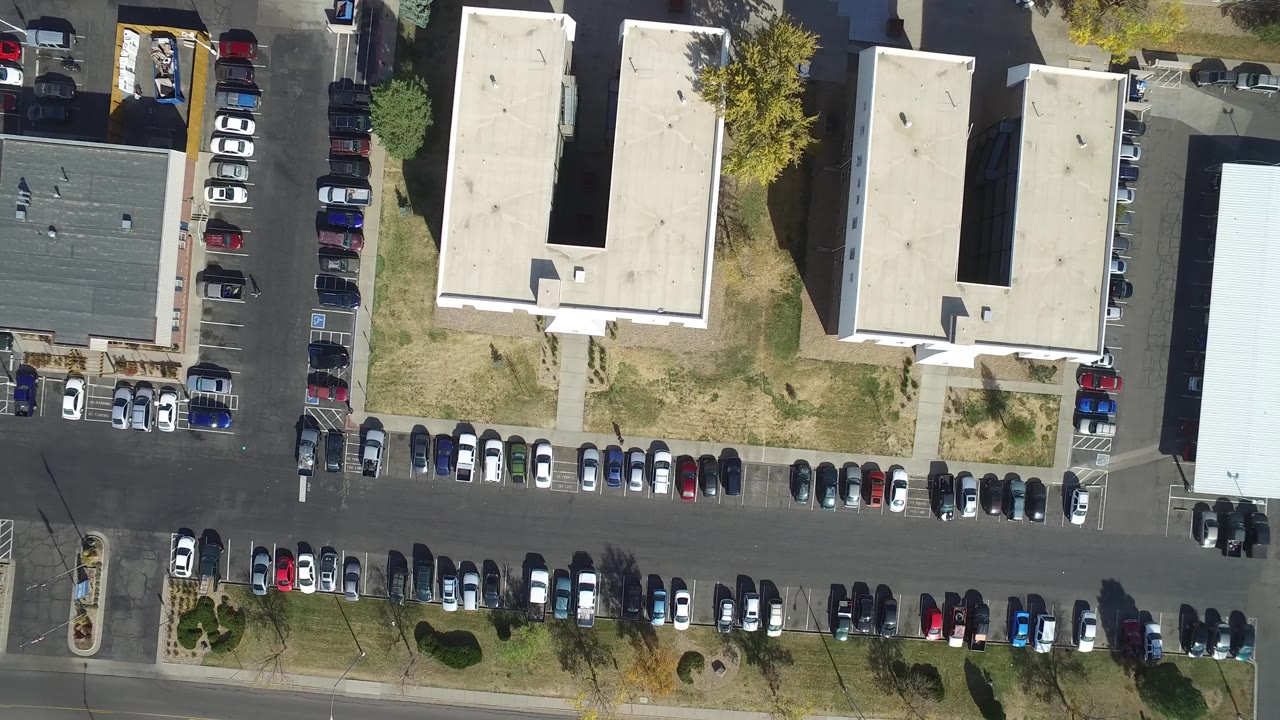 Aerial frame over Hidden Lake, Colorado with long rows of parked cars, pale building roofs, landscaped islands, dry grass, and no visible people.