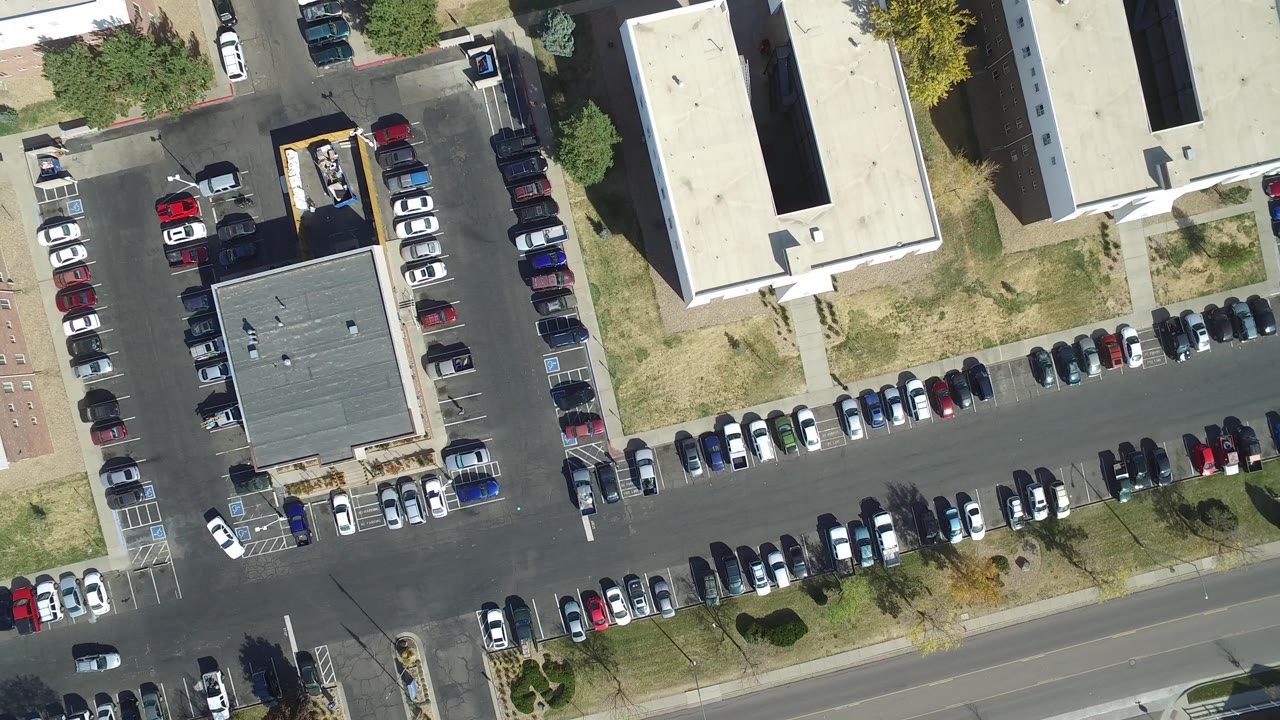 Hidden Lake, Colorado aerial frame with dense rows of parked vehicles, a central dark-roofed structure, light building roofs, grass strips, trees, and no discernible people.
