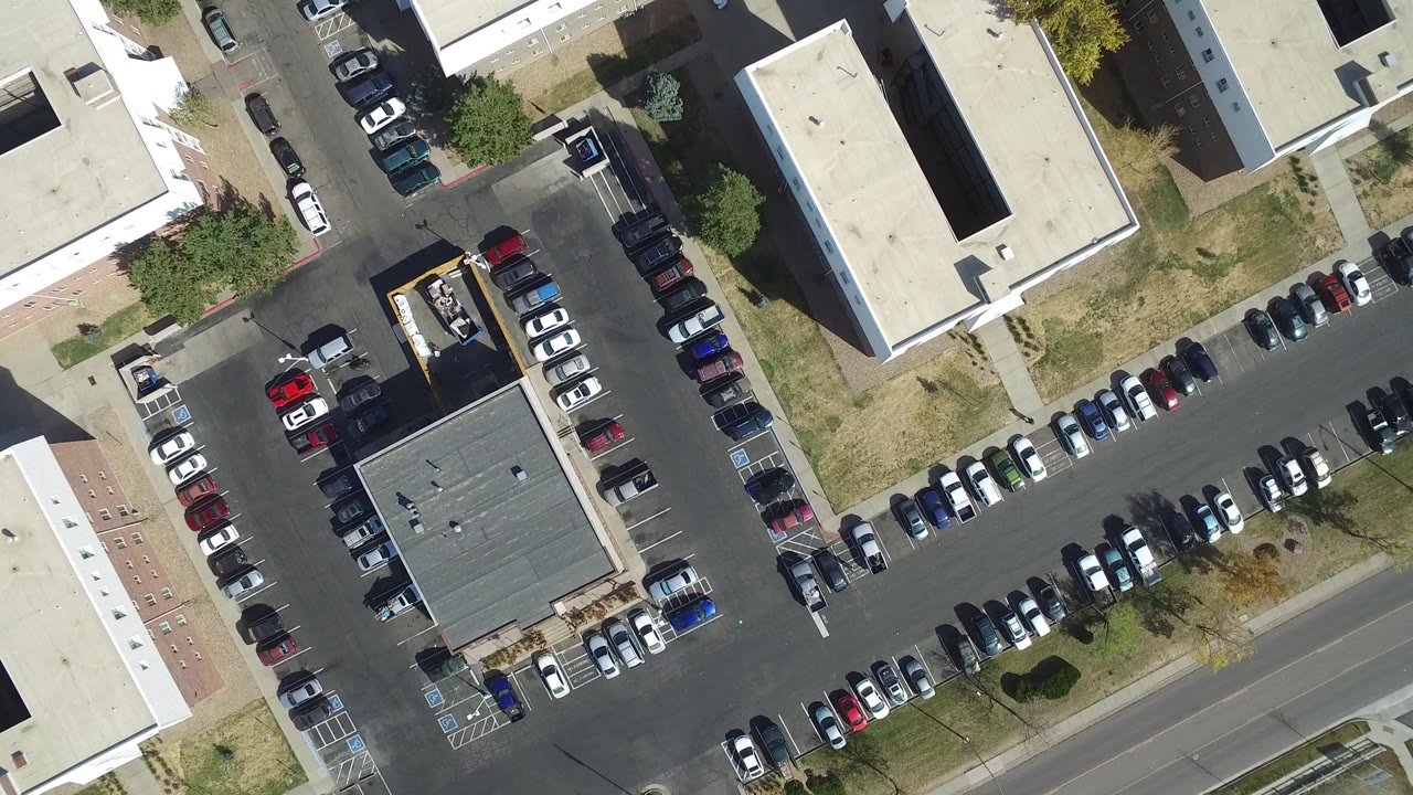 Overhead view of buildings, parking lots, roads, and parked cars.