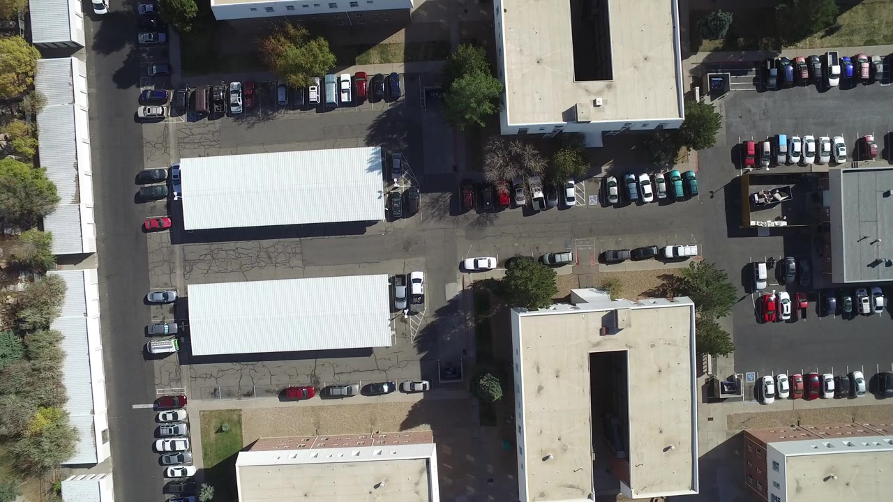 Top-down aerial frame in Hidden Lake, Colorado showing parked cars, asphalt lots, flat-roofed buildings, trees, and no visible people at the start of the clip.