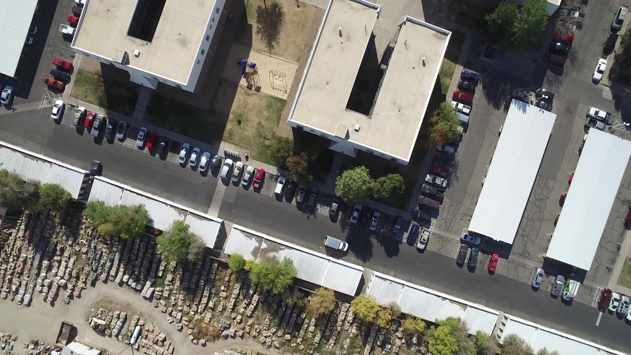 Overhead view of industrial roofs, parked cars, road, and storage yard