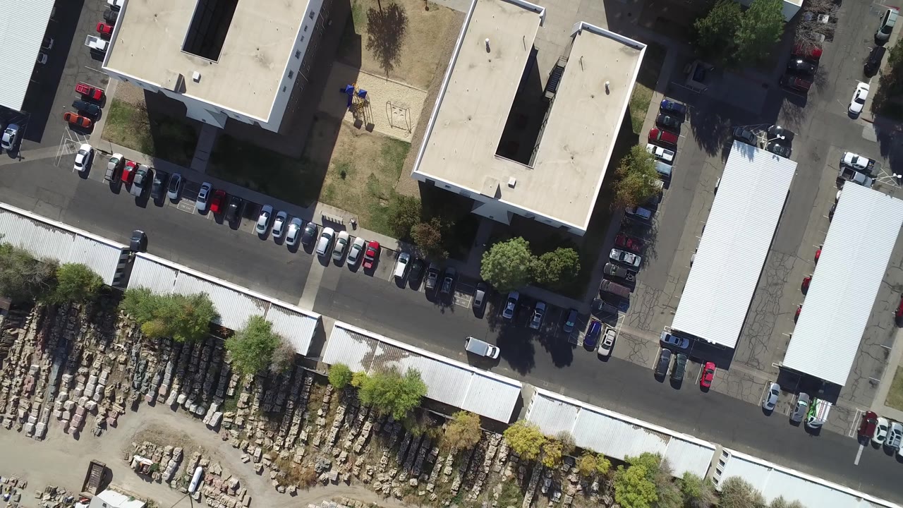 At 0:01, the aerial view over Hidden Lake, Colorado centers on beige industrial rooftops, lined parking spaces, a long light-colored warehouse roof, and stored materials, with no visible people.