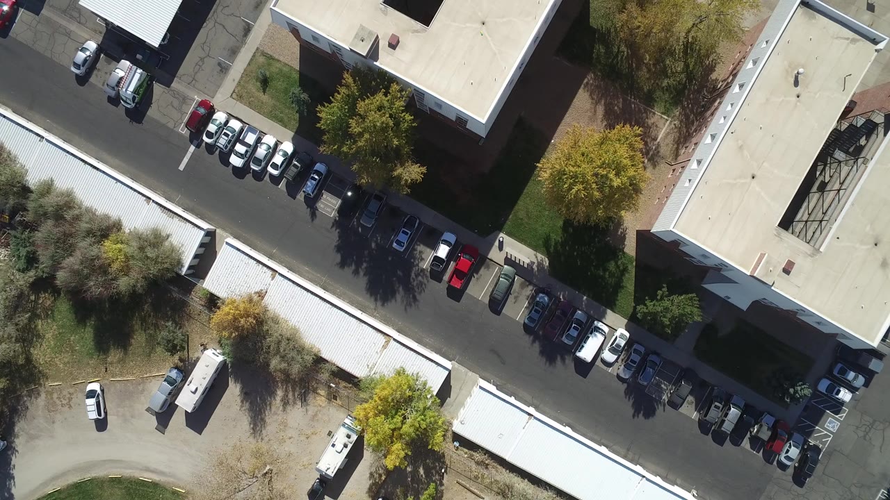Top-down aerial view of buildings, parked cars, roads, and trees.