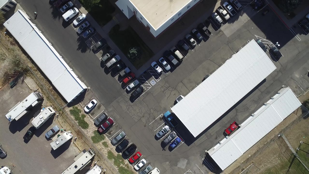 Top-down lot with two white buildings and rows of cars