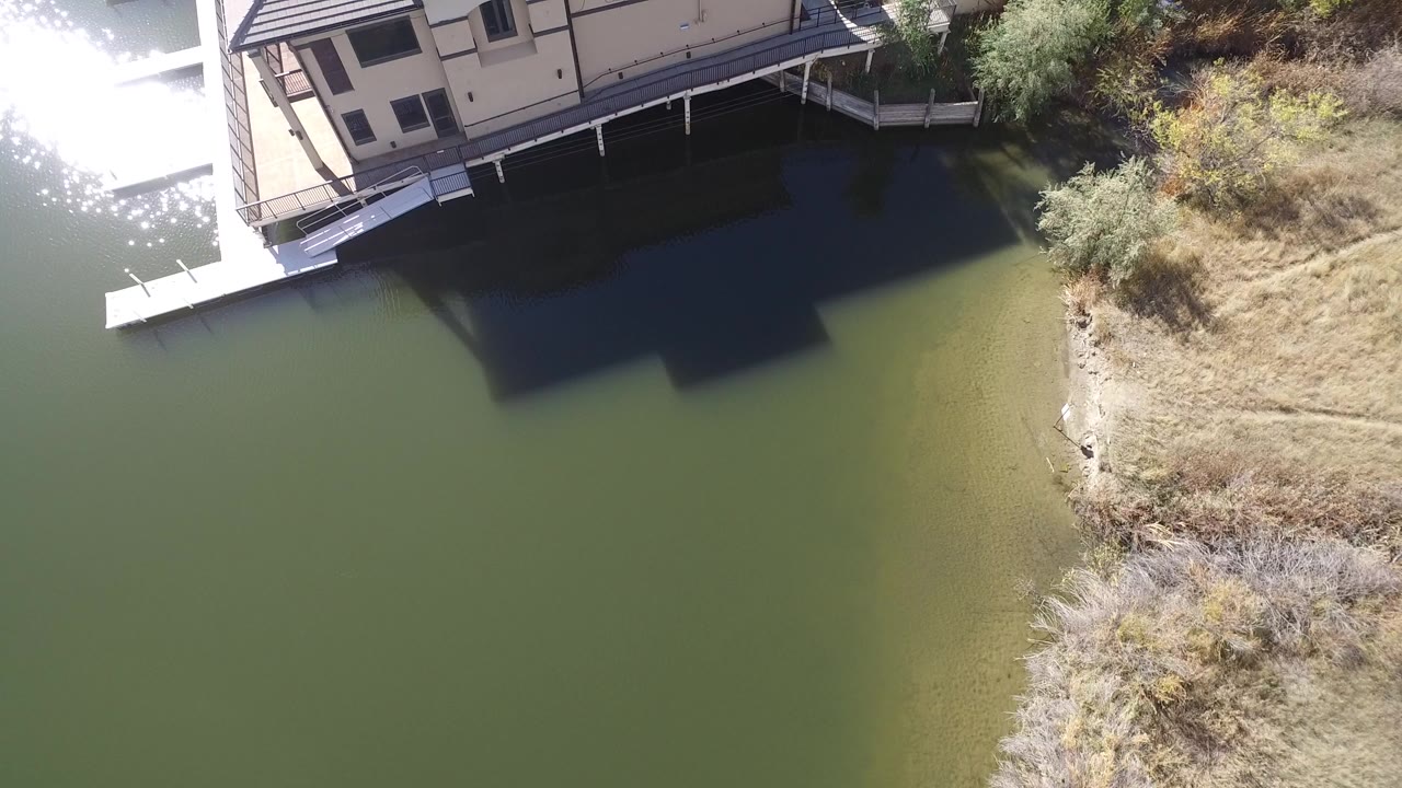 Overhead view of green lake water beside a light-colored lakeside house and dry shoreline.