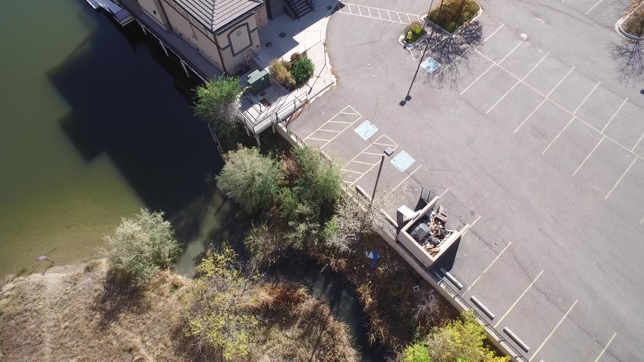 Drone view of a villa corner, green water, and empty parking rows.