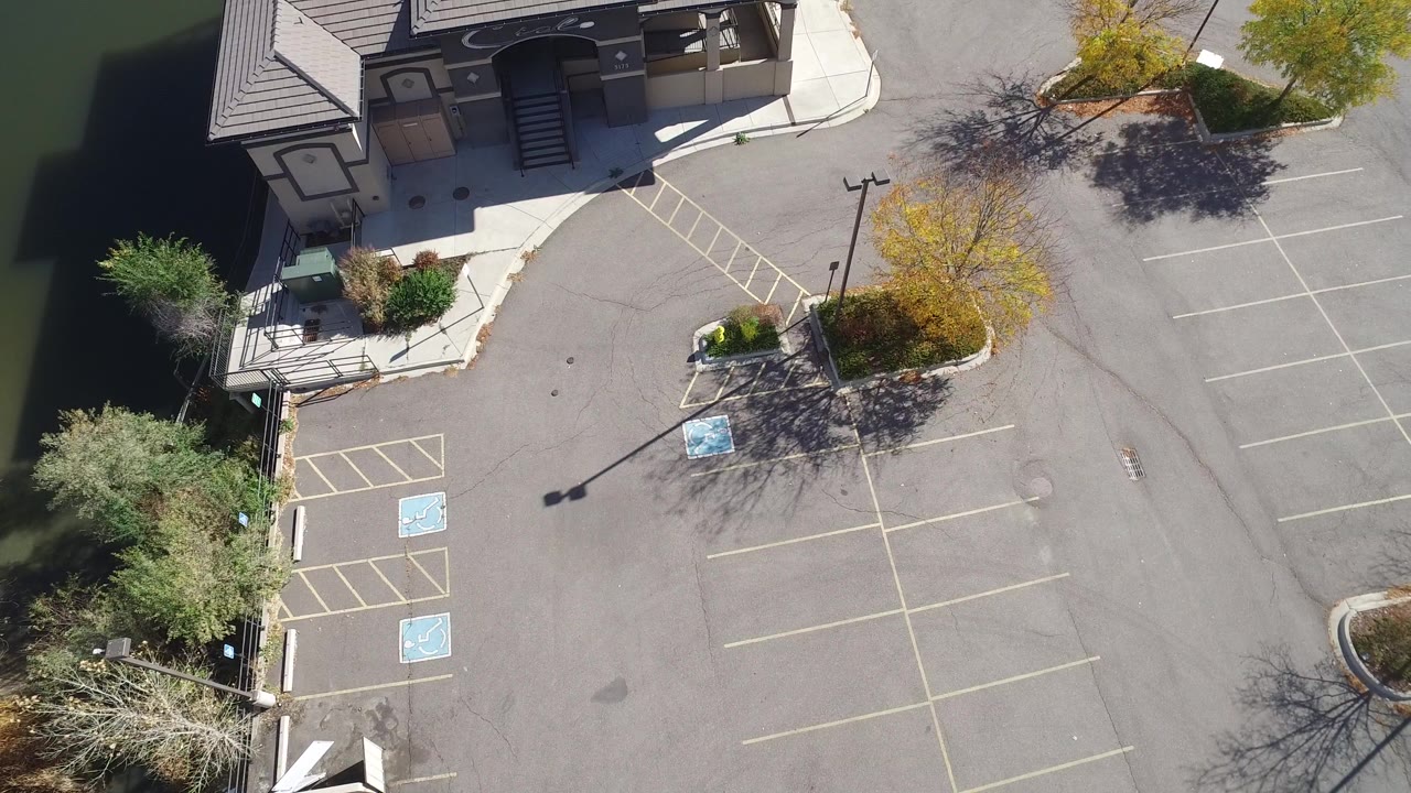 Aerial frame over a Hidden Lake, Colorado building frontage with empty striped parking spaces, accessible markings, landscaped curbs, and no visible people.
