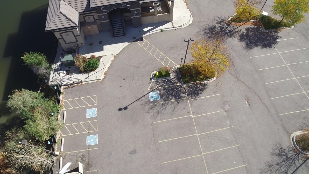 Aerial view in Hidden Lake, Colorado looking across a building entrance area, accessible parking spaces, light poles, landscaped trees, and no visible people.