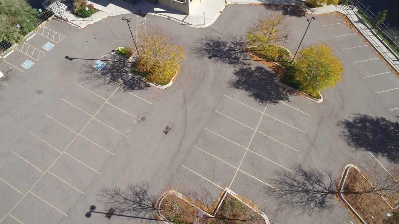 High drone view over an empty parking lot in Hidden Lake, Colorado, with accessible spaces at upper left, autumn trees, asphalt striping, and no visible people.