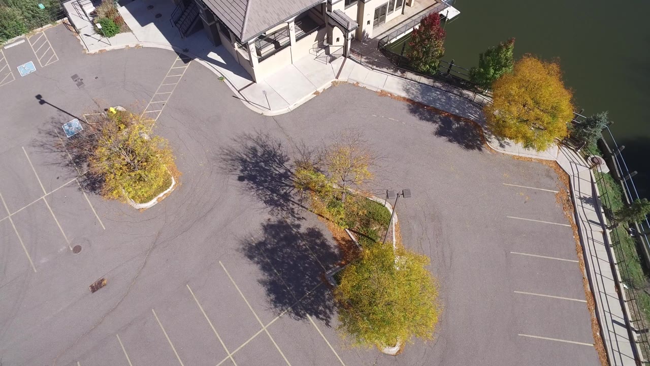 Overhead view of a parking lot beside a light-colored lakeside building and dark water.