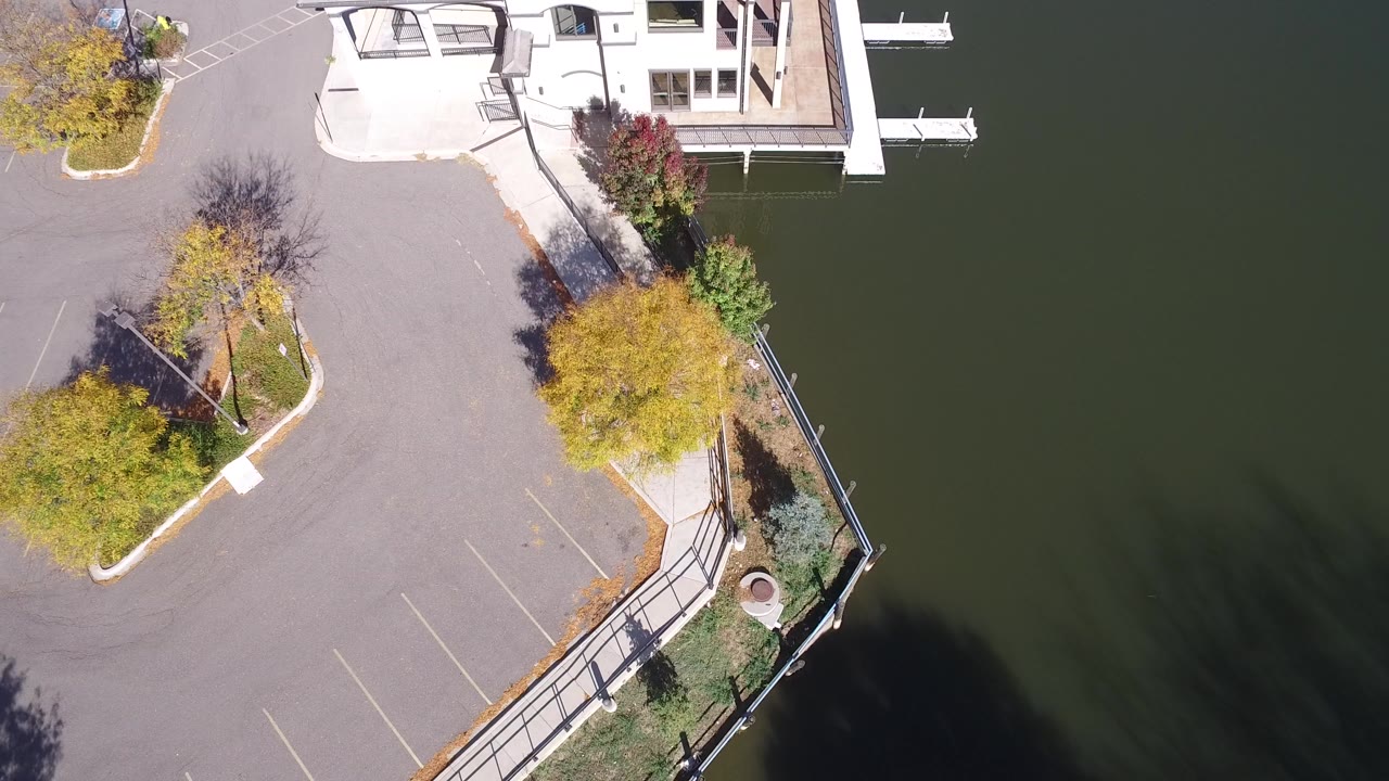 Overhead frame from Hidden Lake, Colorado showing a paved parking area, autumn trees, a railing along the water, part of a house or dock structure, and no visible people.