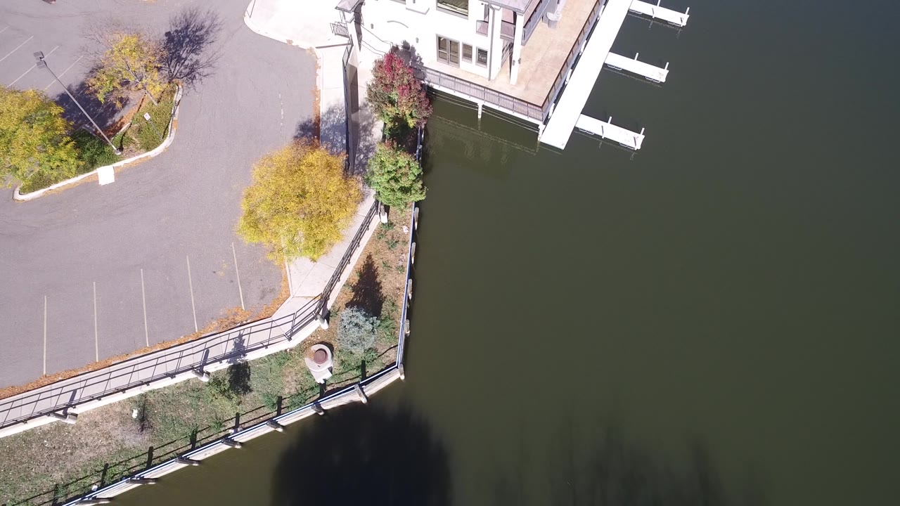 Aerial frame in Hidden Lake, Colorado with the building corner and white dock slips at the top, green water to the right, and parking pavement with trees to the left, with no visible people.