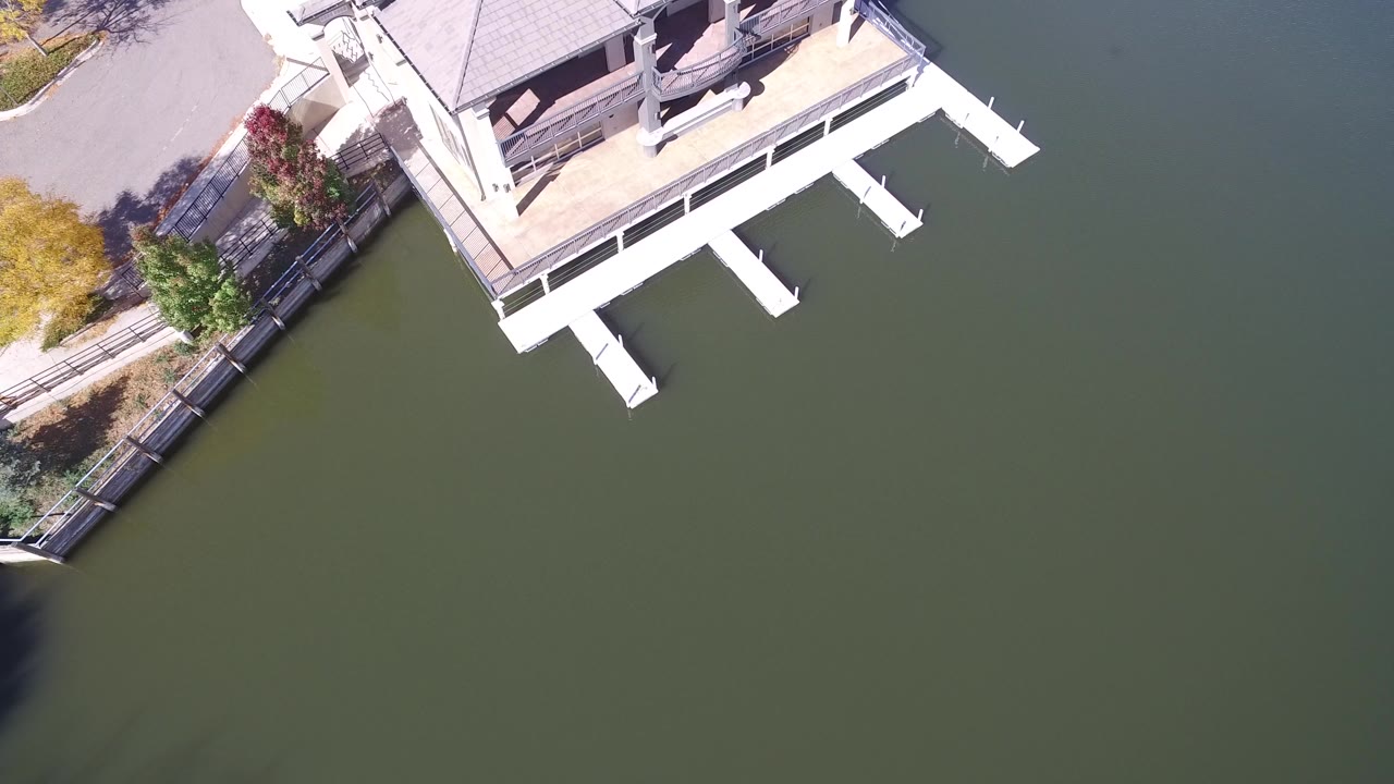 Overhead view of a white lakeside dock and green water.