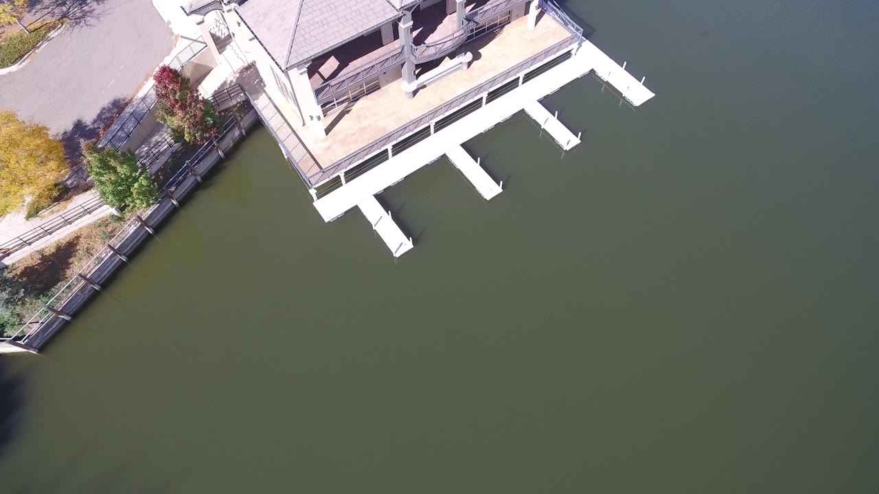 Hidden Lake, Colorado aerial view with white dock supports projecting over green-blue water, shoreline paving, trees, fencing, and no visible people.