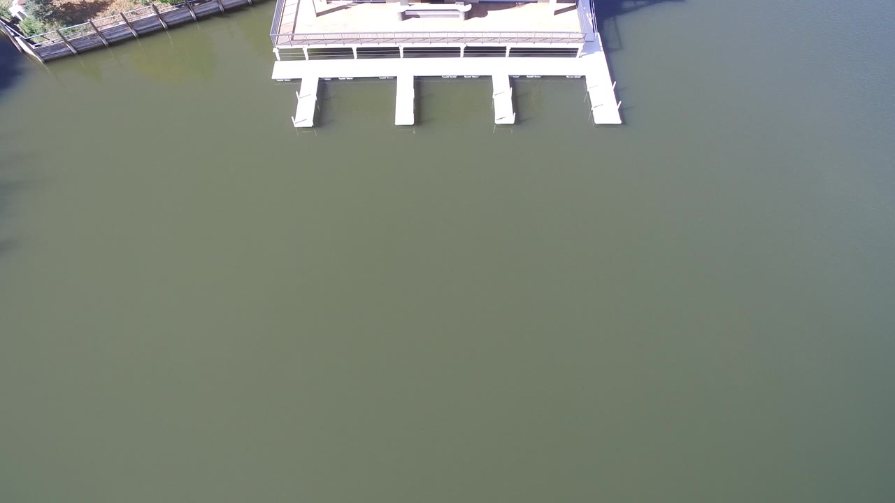 High aerial frame at Hidden Lake, Colorado, showing white dock supports at the top edge and a broad area of calm green-blue water with no visible people.