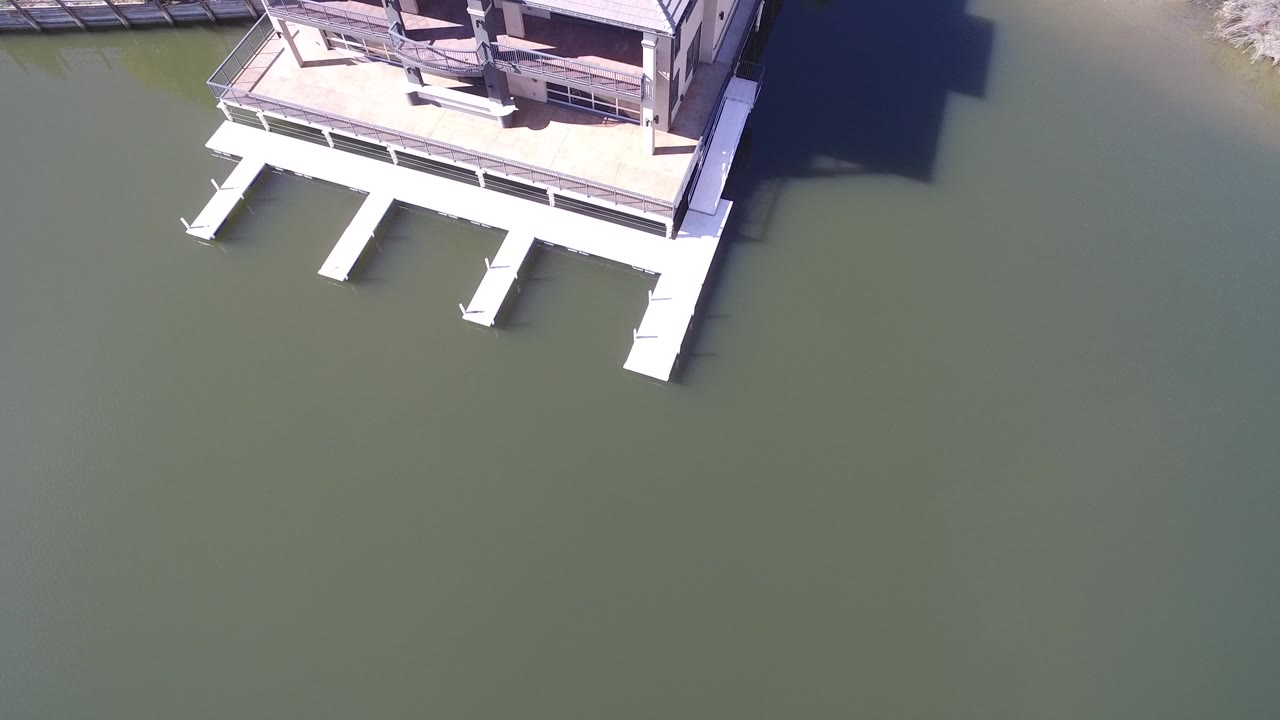 High aerial frame of a Hidden Lake, Colorado house at the top edge with white dock fingers extending into green water and no visible people.