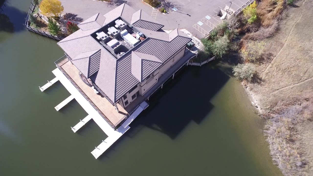Top-down Hidden Lake, Colorado frame showing the house roof, dock fingers, green water, dry shoreline grass, and no visible people.