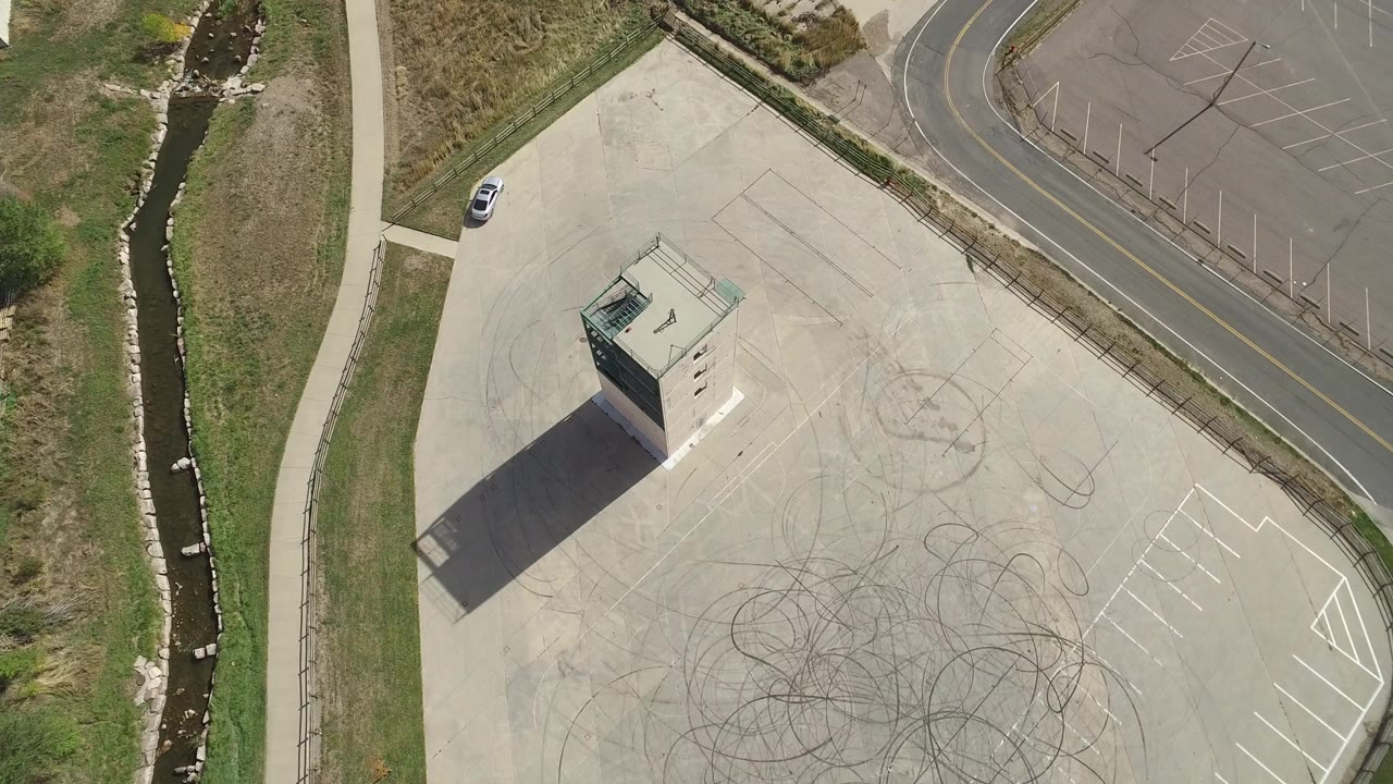 Overhead view of a small structure on a large paved lot beside grass and a creek.