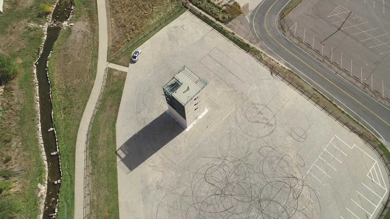 Top-down frame in Hidden Lake, Colorado with the small structure slightly left of center, tire arcs across the pavement, a curving road above, and no visible people.