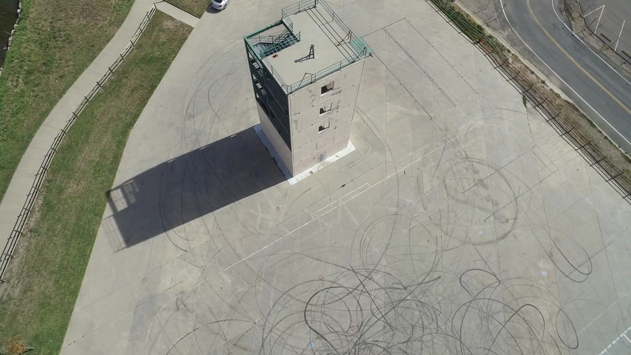 Aerial tower view with fenced roof, road edge, and marked concrete.
