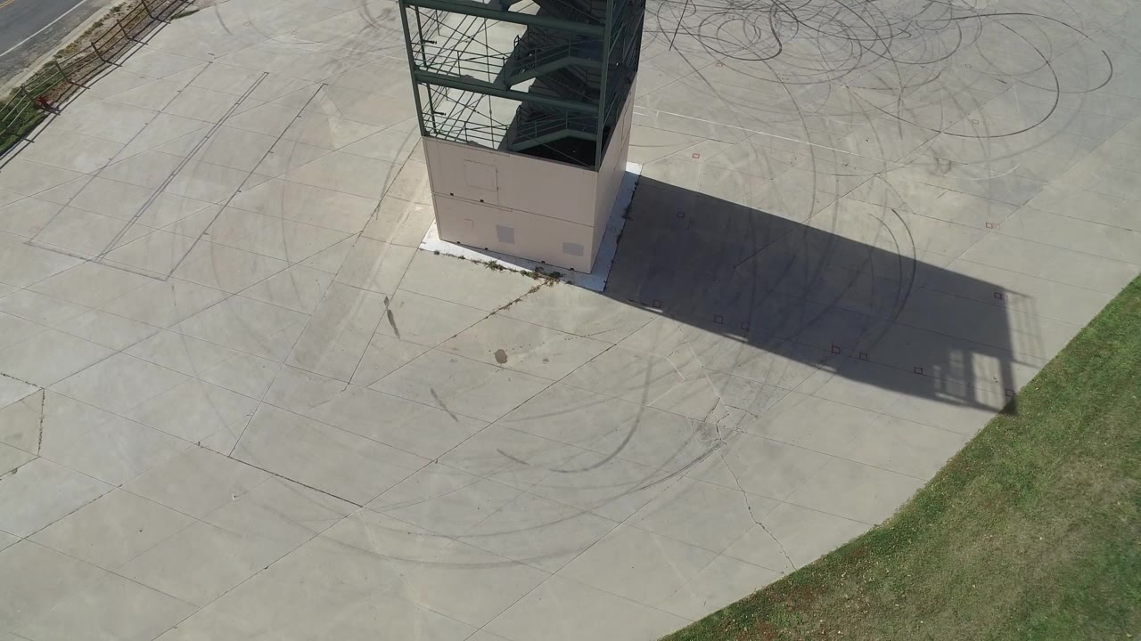 Overhead view of a metal tower casting a shadow across pale concrete.