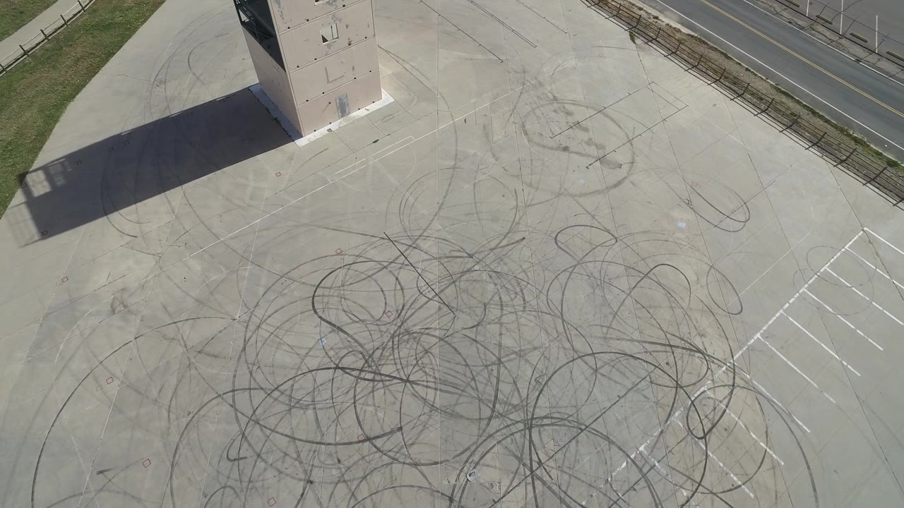 Aerial view of a paved lot with dense tire loops and parking stripes at right.