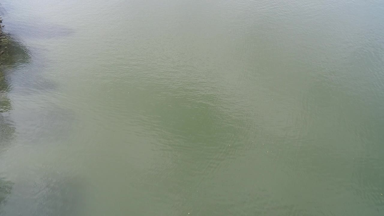 Muted green lake water with cloud reflection and faint diagonal ripple marks.