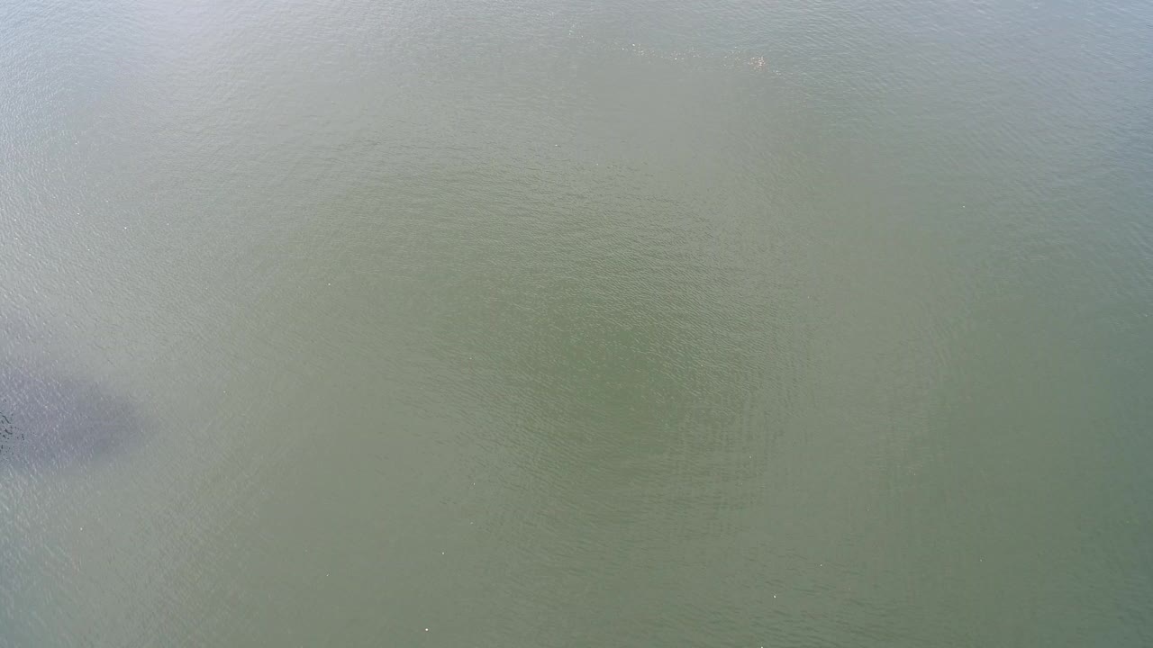 Overhead view of green-blue water at Hidden Lake, Colorado, with soft surface texture, a darker patch near the left edge, and no visible people.