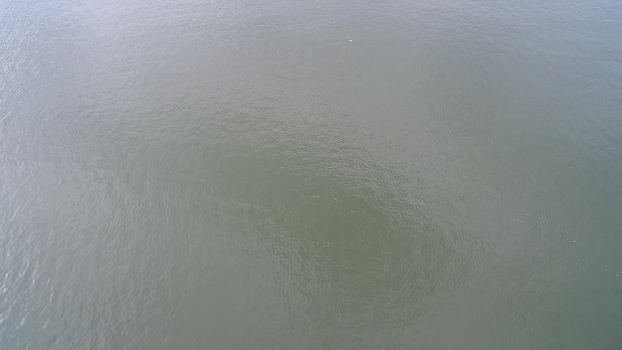 Top-down Hidden Lake, Colorado water surface with muted green-gray color, light ripple lines, faint darker areas under the surface, and no visible people.