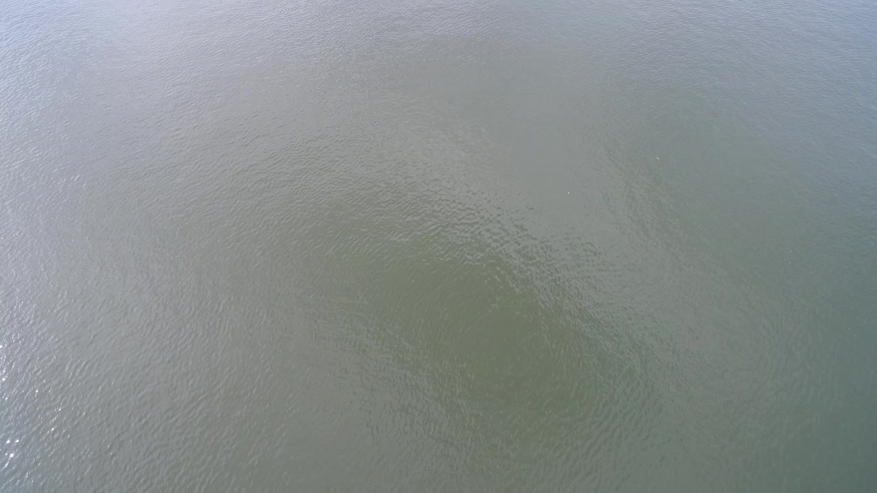 Aerial view of rippling green-blue lake water with cloud reflection.
