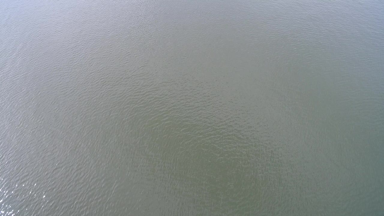 Top-down view of rippled water at Hidden Lake, Colorado, with muted green-brown color, pale surface reflections, and no visible people.