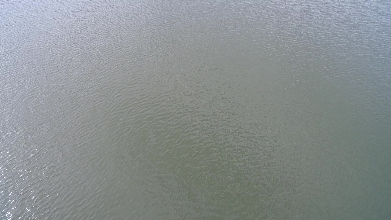 Hidden Lake Colorado water fills the frame with fine ripples, a brighter reflective streak left of center, faint darker shapes under the surface, and no visible people.
