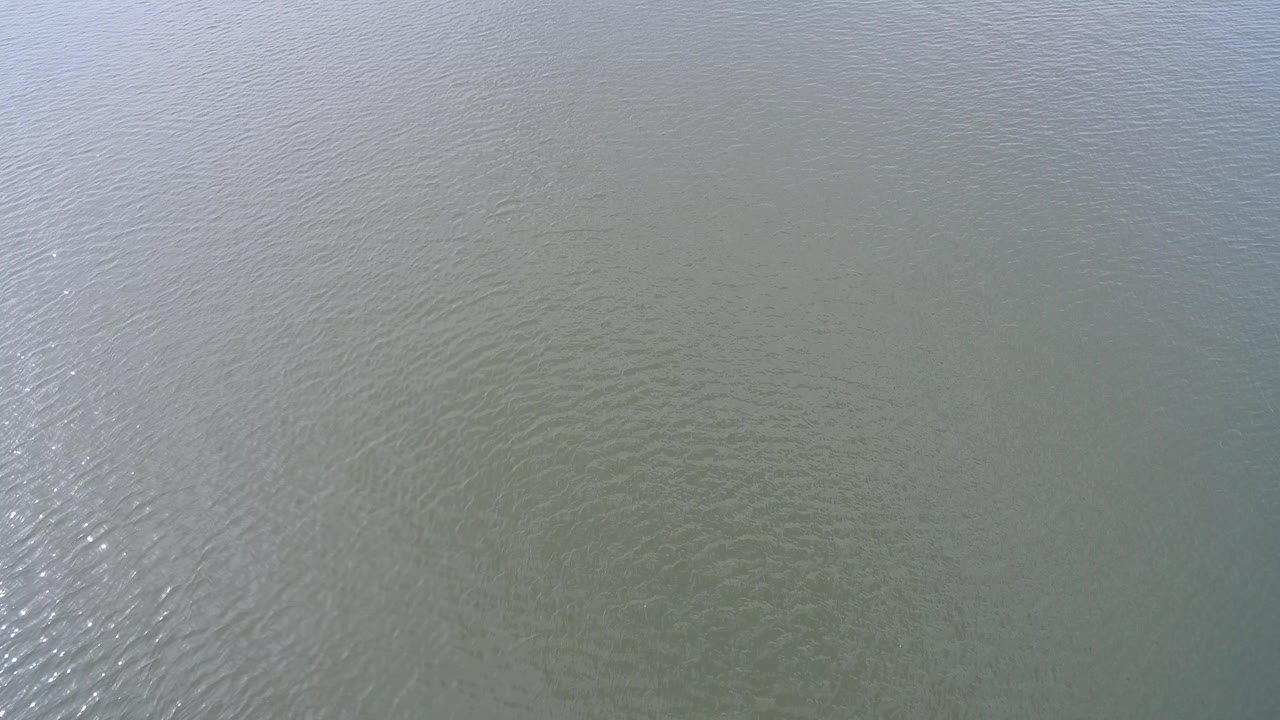 Overhead view of pale green-gray water at Hidden Lake, Colorado, with fine ripples and a bright reflected band near the center, no visible people.