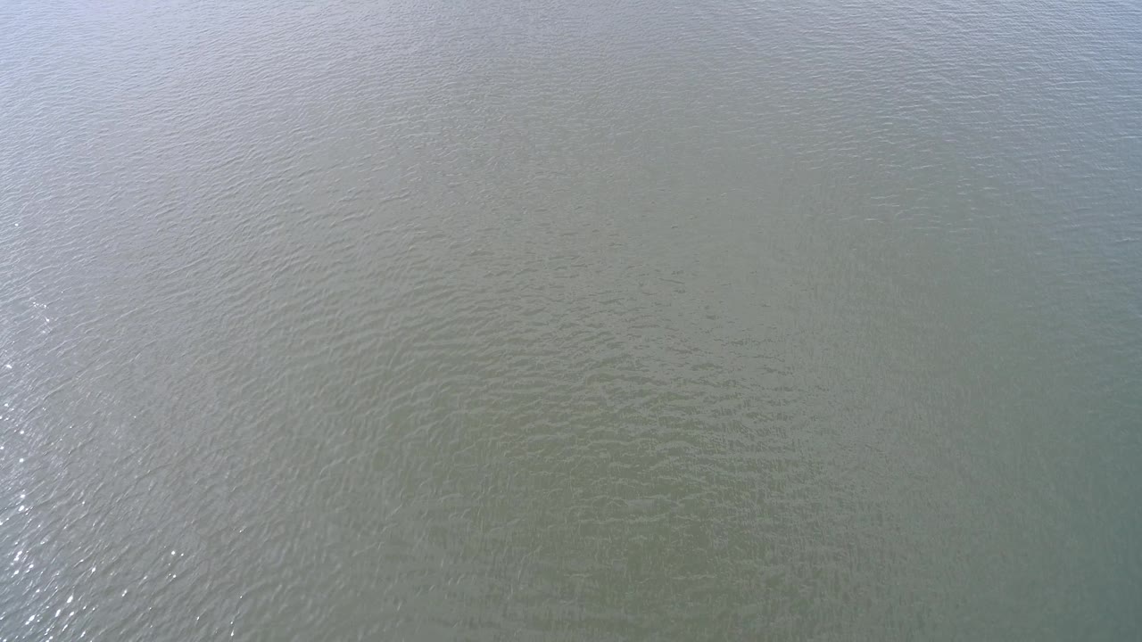 Open Hidden Lake water fills the frame with small wave patterns, muted green-gray color, and a soft vertical patch of glare, no visible people.