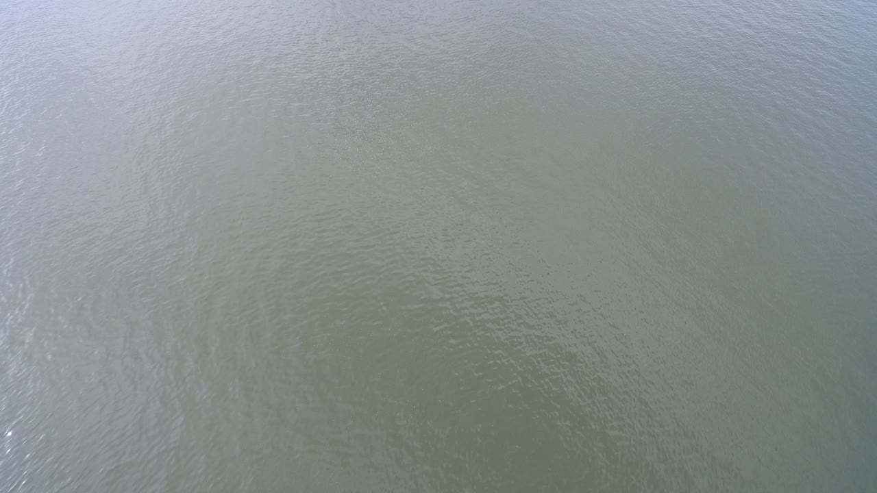 Aerial frame of Hidden Lake, Colorado showing muted gray water with thin ripple lines and a pale reflective patch, with no visible people or boats.