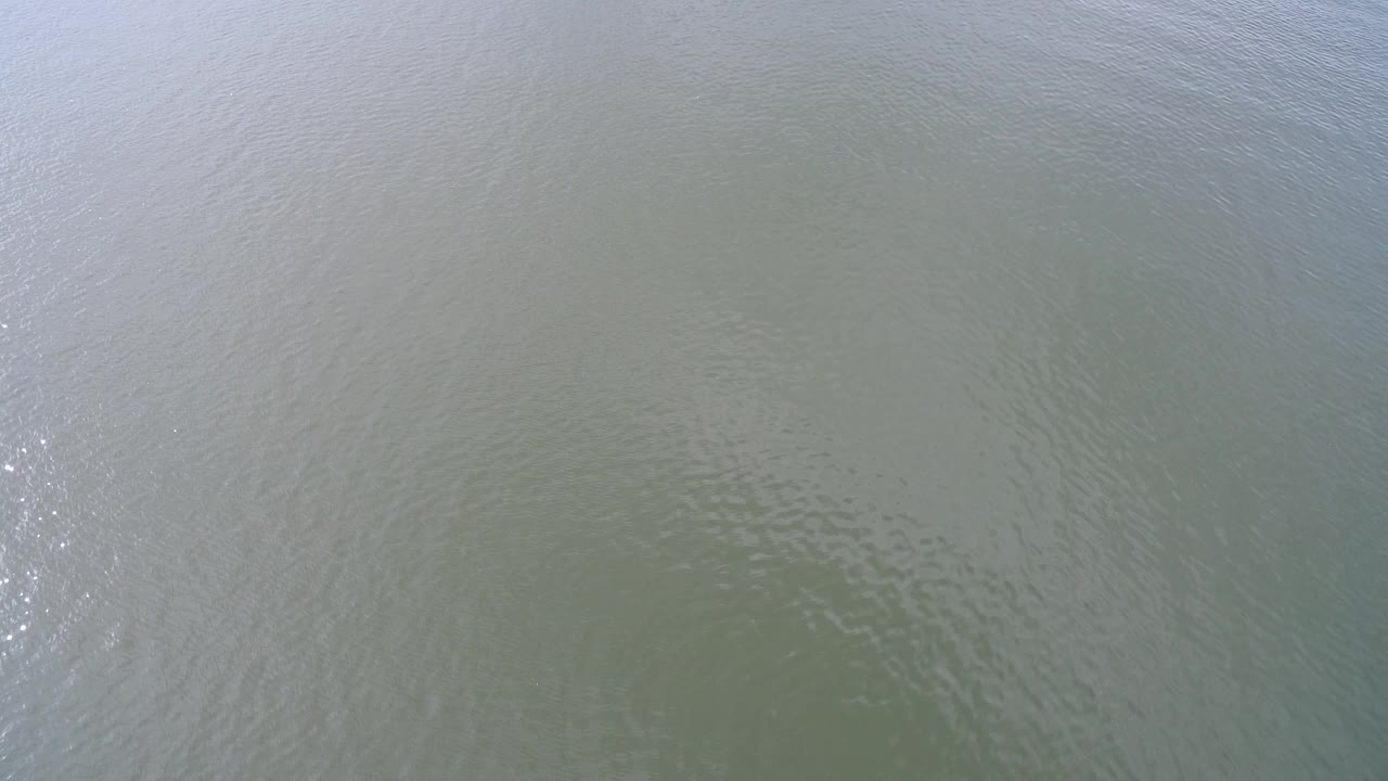 Overhead aerial view of rippled brown-green river water in Hidden Lake, Colorado, with bright sun glints near the left edge and no visible people.
