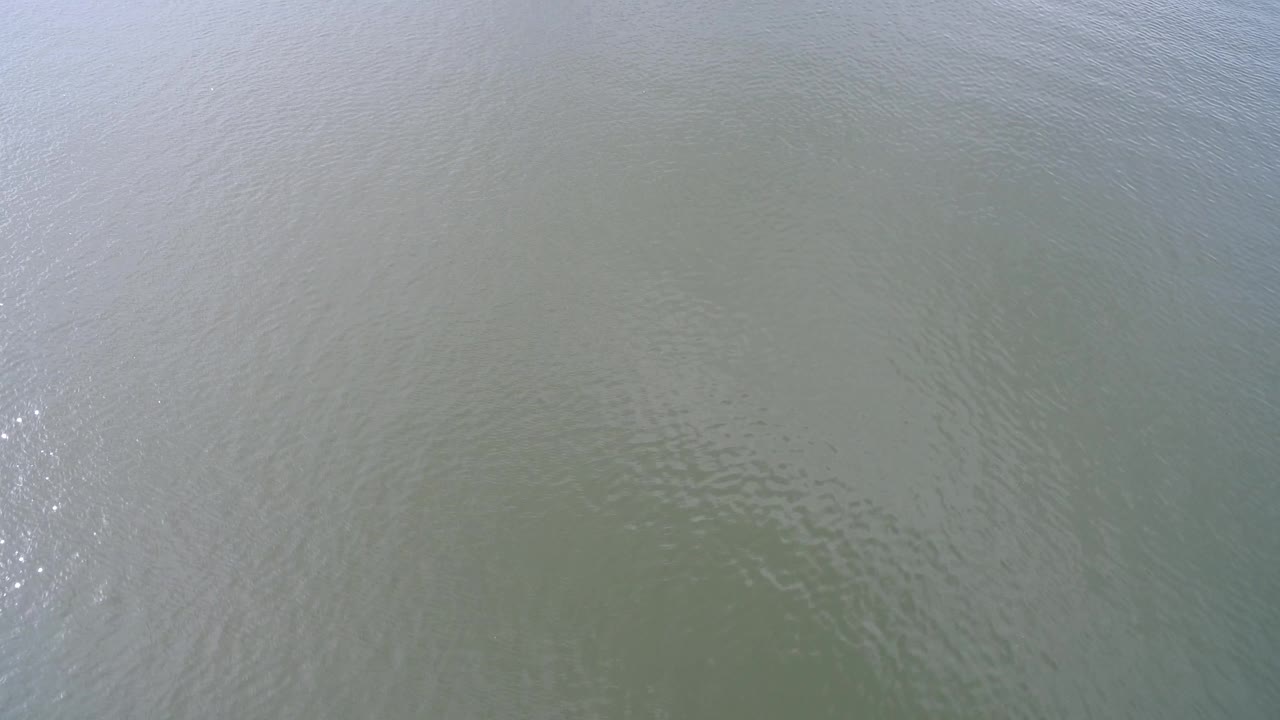 Overhead frame of Hidden Lake, Colorado river water with fine ripples, muted brown-green color, and a small band of reflected sunlight, with no visible people.