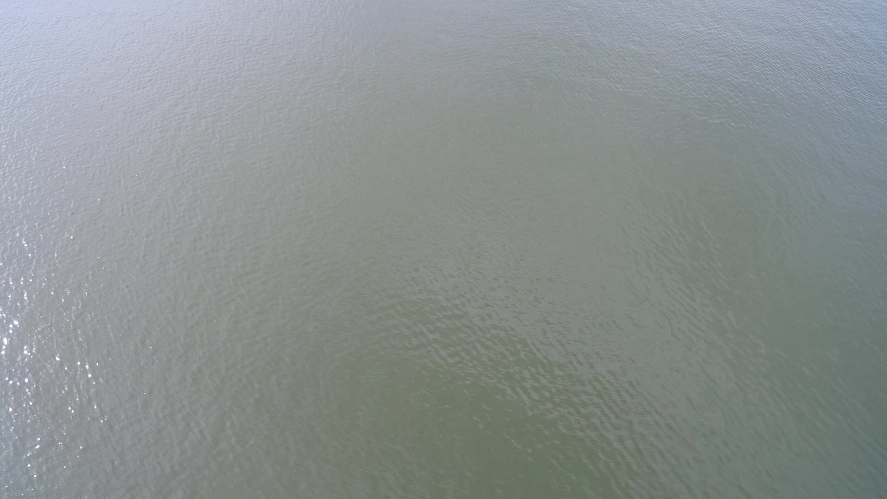 Overhead Hidden Lake water surface with muted green color, small wave patterns, a brighter vertical patch of reflected light near center, and no visible people.