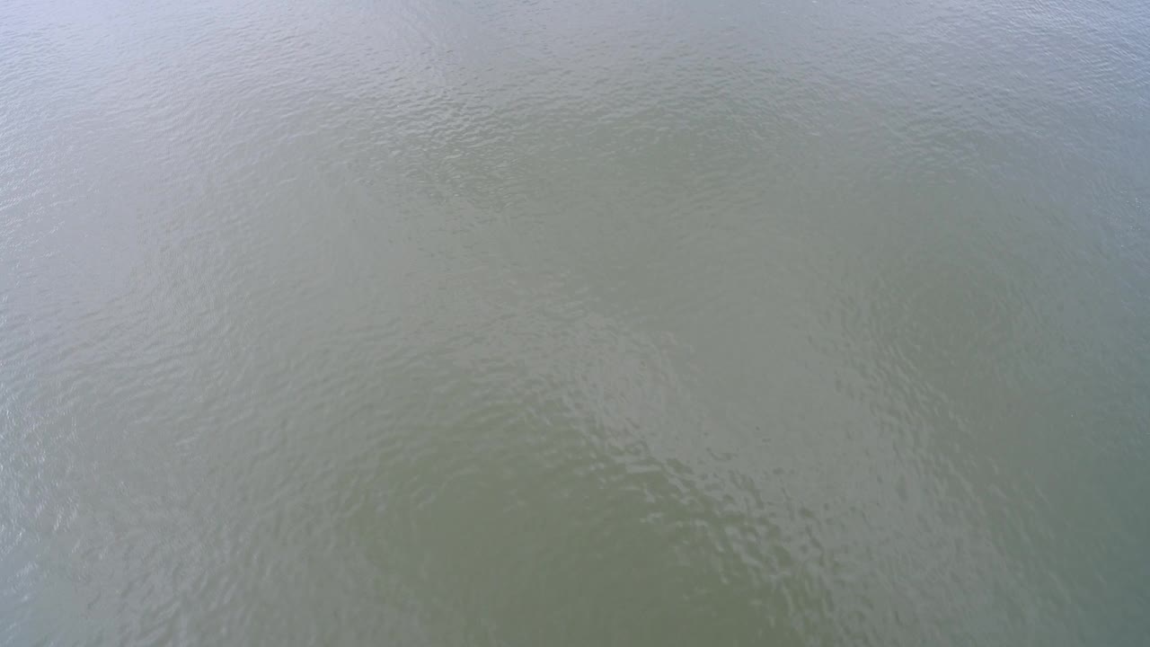 Top-down aerial view of green-gray water at Hidden Lake, Colorado, with faint ripples and soft reflection across the surface, no visible people.