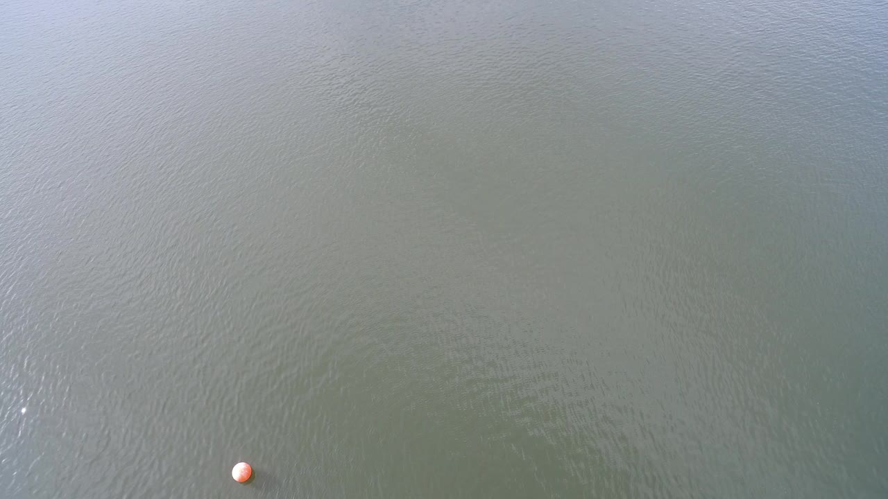 Aerial view over Hidden Lake, Colorado showing rippled green-gray water, faint reflected light, and a small orange buoy near the lower left edge with no visible people.