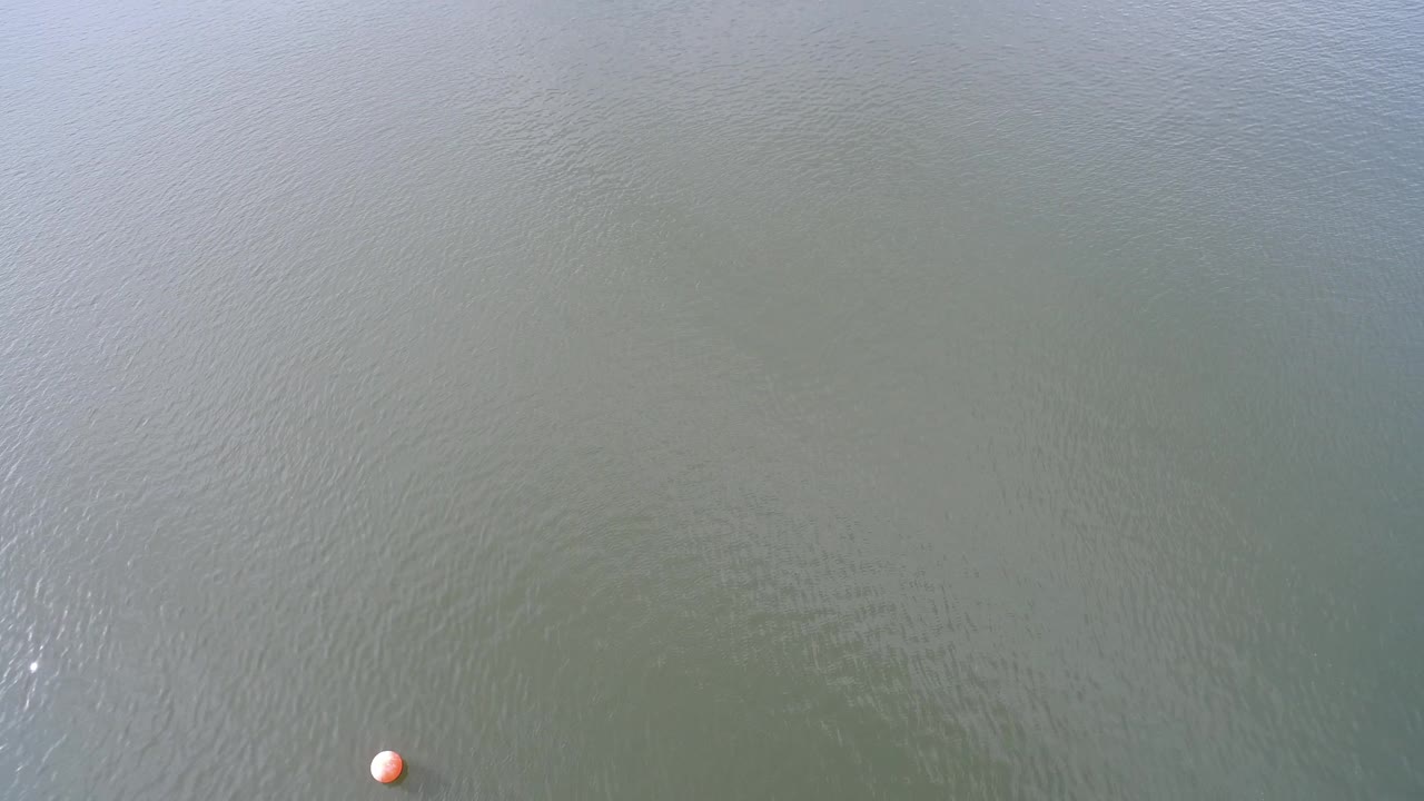 Aerial frame from Hidden Lake, Colorado with pale green-gray rippled water and the orange buoy shifted closer to the lower center, with no visible people.