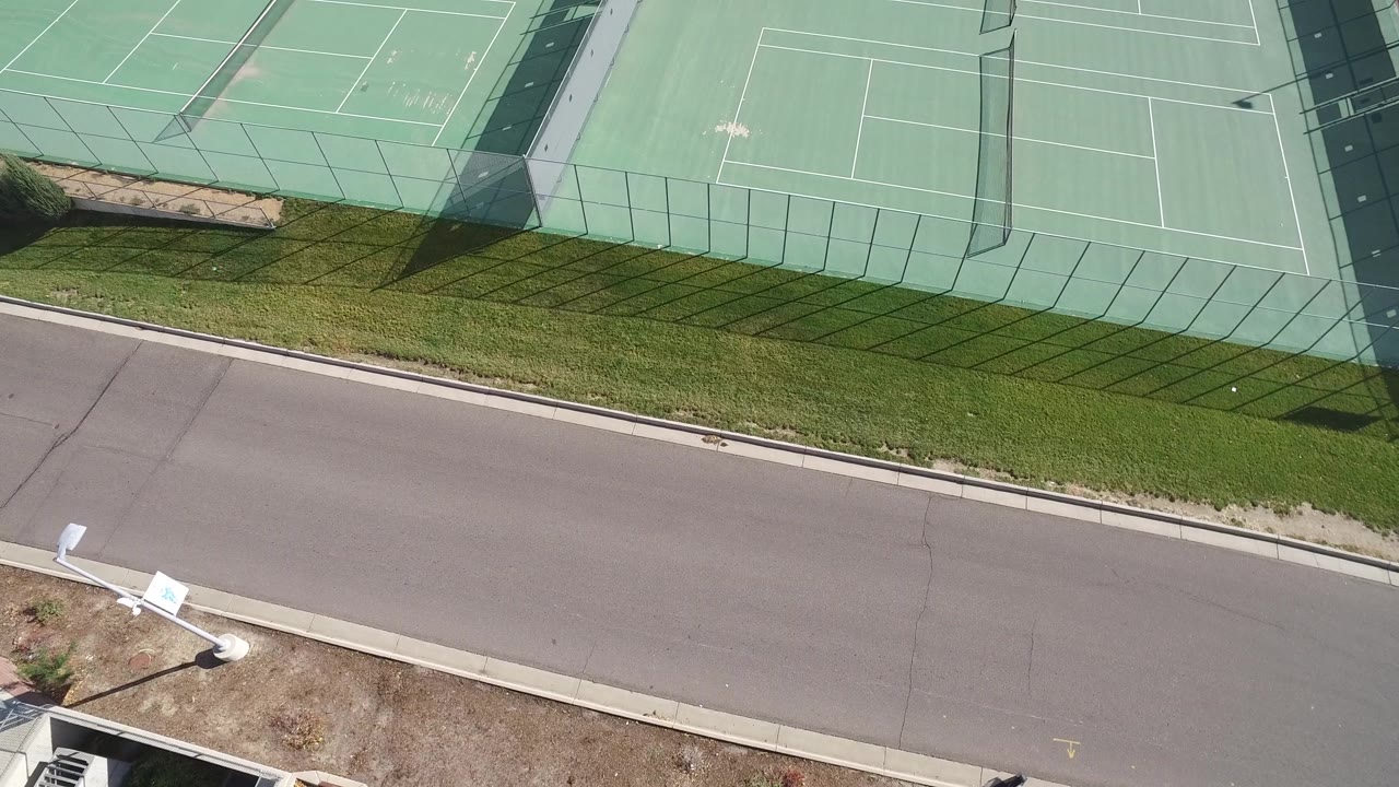 Top-down view of tennis court fencing casting shadows onto grass.