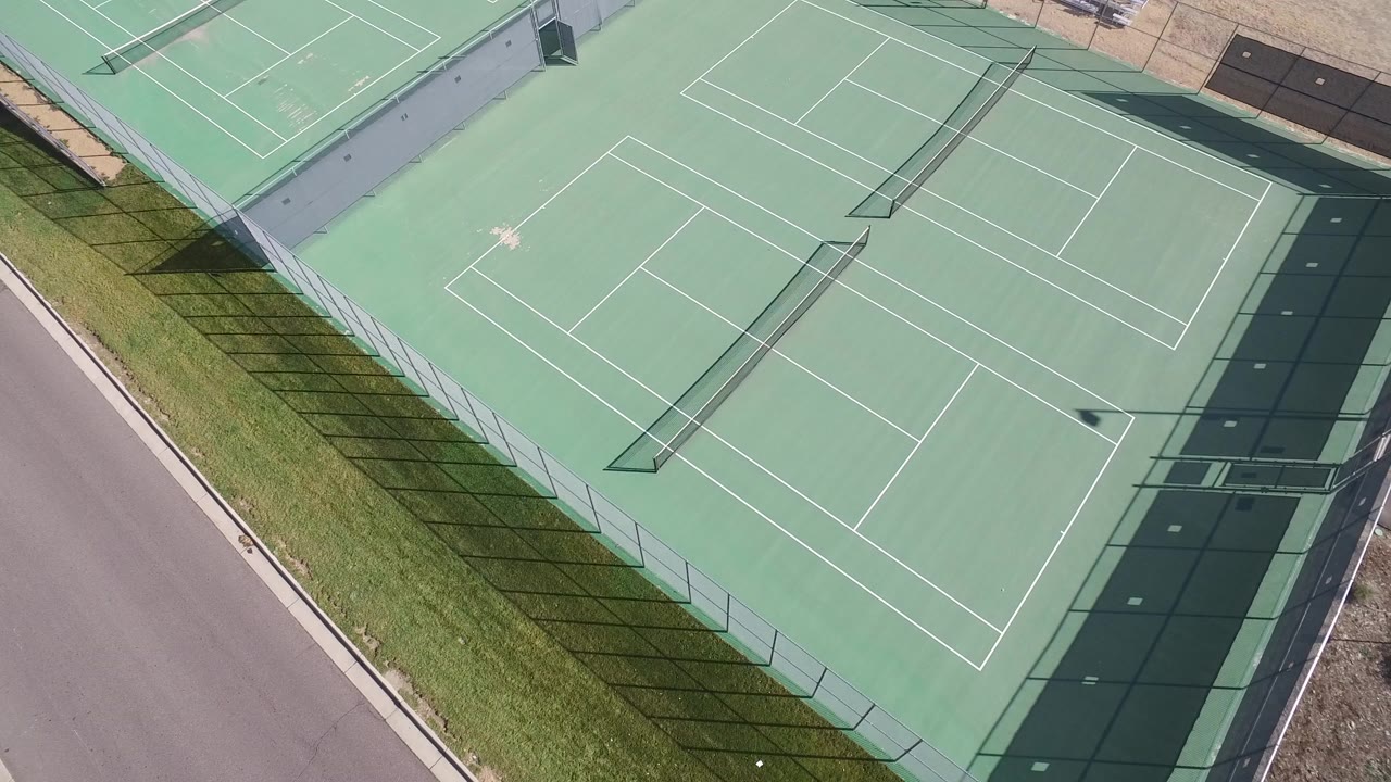 Overhead view of a green fenced tennis court beside a road.