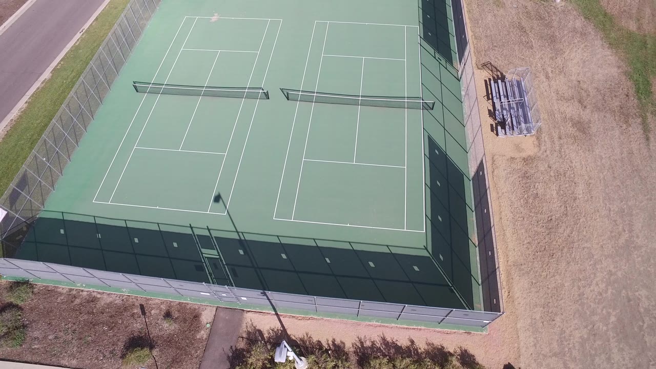 Aerial frame in Hidden Lake, Colorado showing empty green tennis courts, white striping, fence shadows, tan ground, and no visible people.