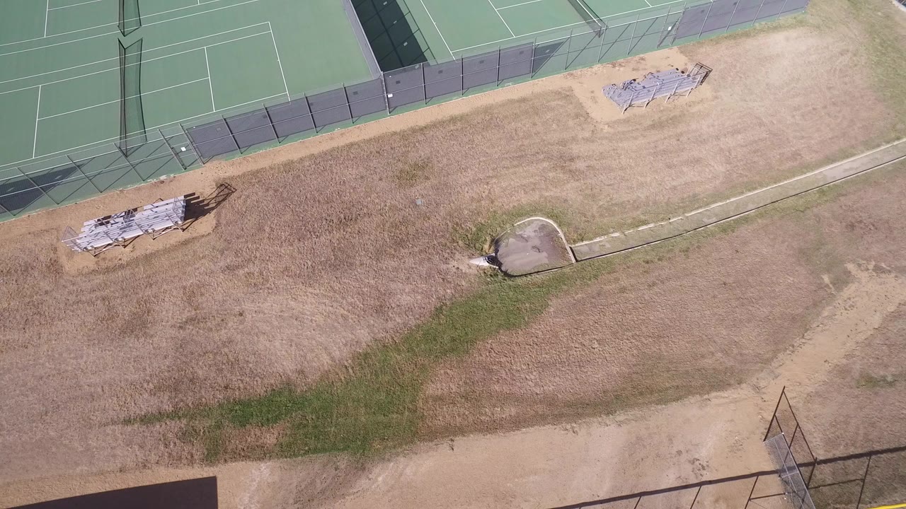 Overhead frame in Hidden Lake, Colorado showing green fenced tennis courts at the top, dry tan ground below, stacked materials near the court edge, and no visible people.
