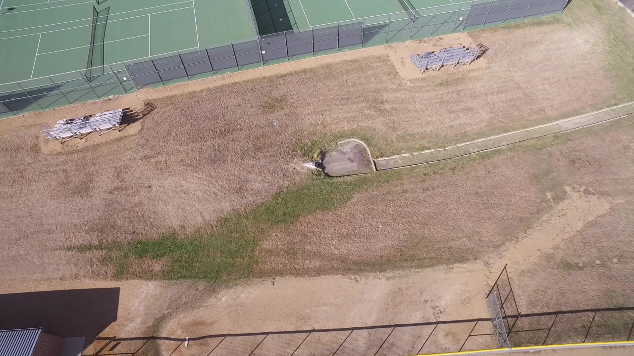 Top-down view of tennis courts, fencing, and dry open land.