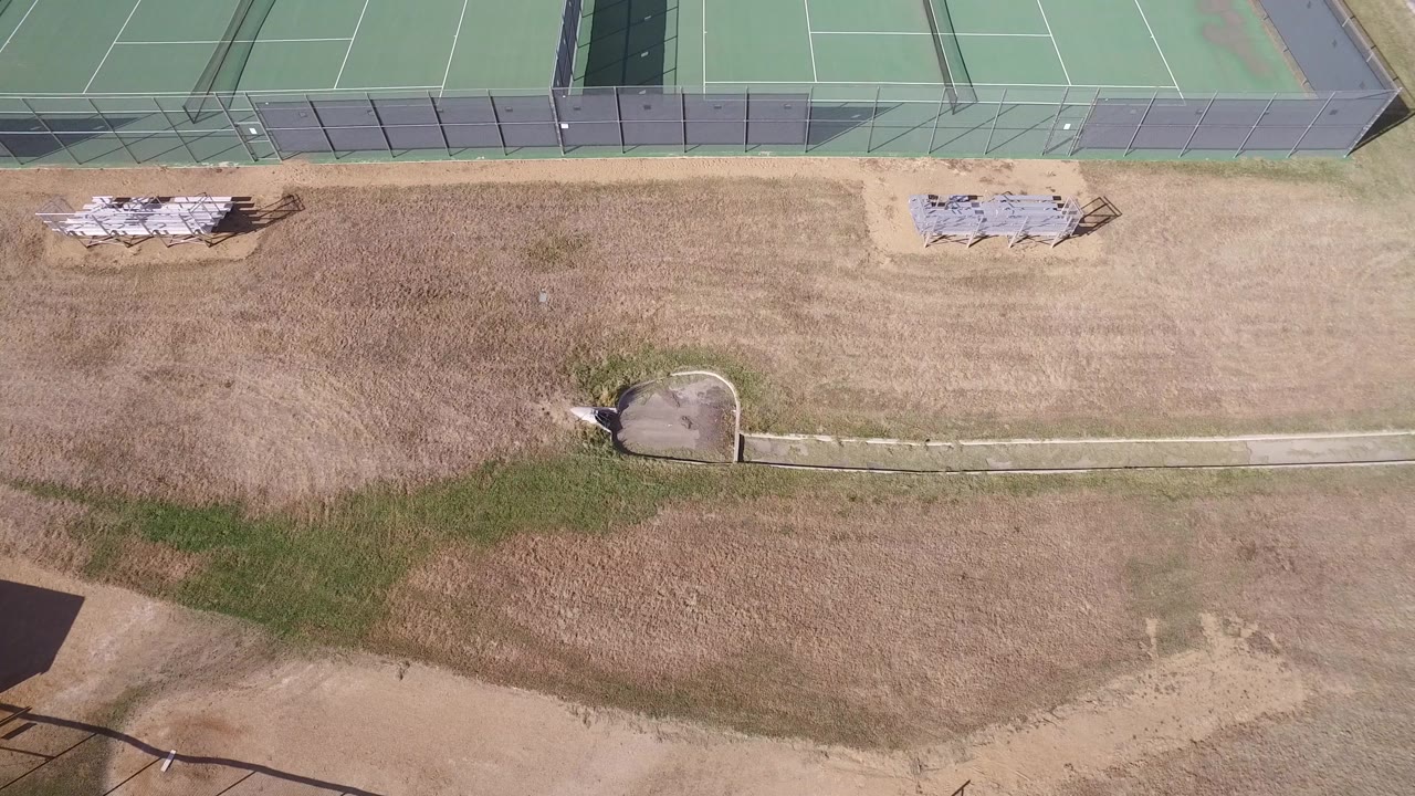 Hidden Lake, Colorado aerial frame with fenced green tennis courts across the top, tan grass through the center, bleachers near the upper edge, and no visible people.