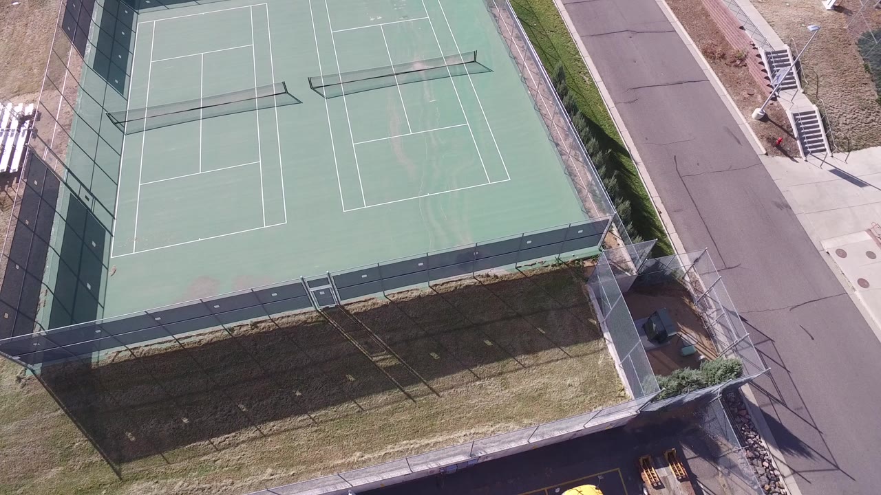 Overhead view of empty double tennis courts beside a road.